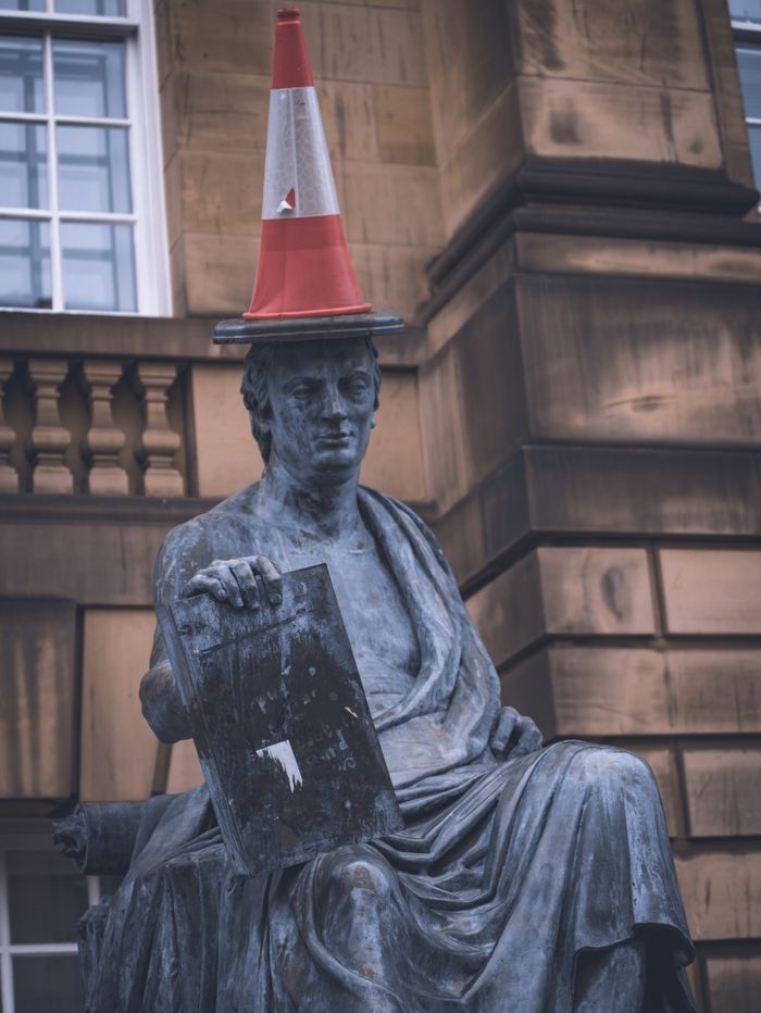 A statue humorously adorned with a traffic cone in an urban environment.
