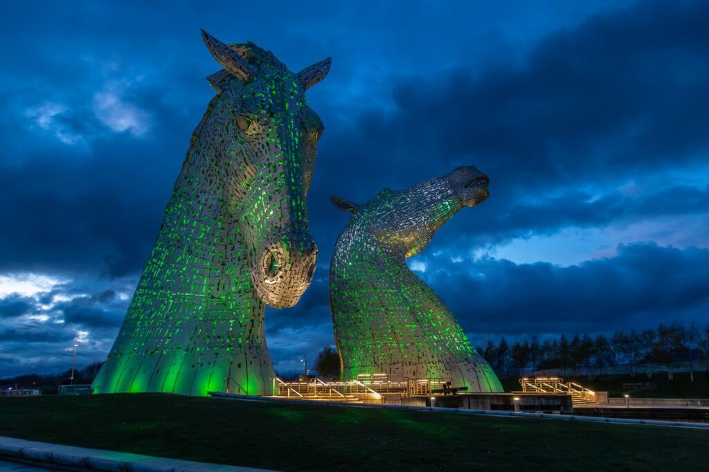 Night view of The Kelpies sculptures in Grangemouth, illuminated against a dramatic sky.